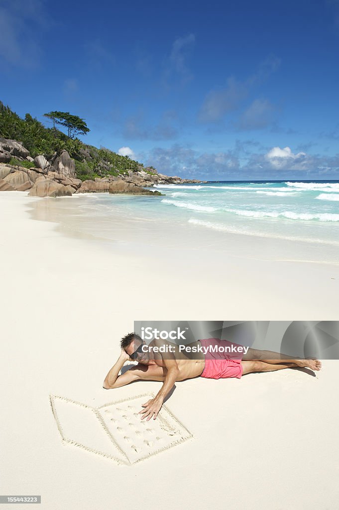 Homem em Calções cor-de-rosa encontra-se na praia com areia Laptop - Foto de stock de Adulto royalty-free