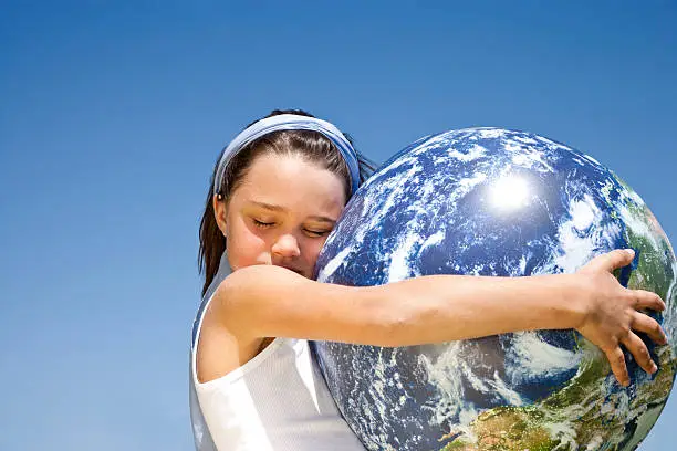 little girl holding globe in her arms, eyes closed, against blue sky