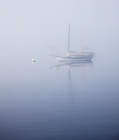 Several sailboats partially obscured by thick, early morning, hazy fog are moored in tranquil Lunenburg Harbor. The waterfront port town of Lunenburg - a UNESCO World Heritage Site - is located on the southern coast of Nova Scotia, Canada near the city of Halifax.