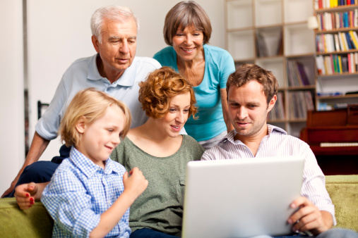 A lovely family with three generation is making plans for the future, looking on a laptop in an luminous indoor scene with out of focus bookshelf in the background. Selective focus on young adults.