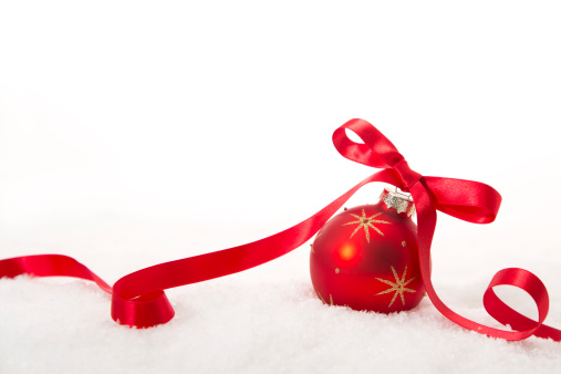 Elegant Christmas bauble with bow nestled in the snow on a white background.