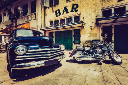 An old chevrolet and a motorbike in front of a bar in Jakarta