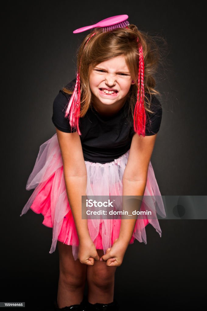 Young angry, rude girl with hair brush and artificial braids 9 years old girl which looks like a doll is angry, she has clenched teeth and fists. Hair brush in hair, artificial braids, Black background, studio shot. 8-9 Years Stock Photo