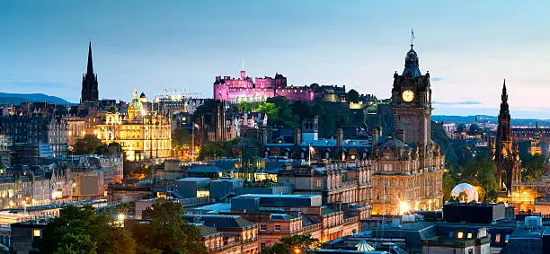 Looking across the city of Edinburgh from Calton Hill at dusk. The Scott Monument, Balmoral Hotel and an illuminated Edinburgh Castle can all be seen.