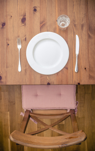 empty plate with a glass of water in front of an empty chair in wood from above