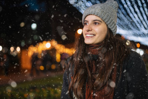 Smiling woman standing in front of illuminated carousel on a Christmas market.