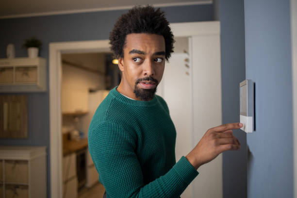 istock Young man adjusts the temperature at home with a device on the wall 1554523634