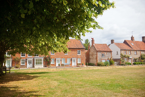 A row of architecturally typical cottages alongside the village green in the popular tourist location of Burnham Market in North Norfolk in East Anglia. The village has many Georgian style properties and the ubiquitous locally quarried building block of so many Norfolk cottages, properties faced in hand-knapped flint stones, as can be seen in the cottages to the right.  Many of the properties are available to rent for holidays.