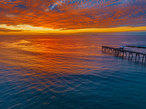 Sunrise seascape with cloud filled sky and the old coal loading jetty at Catherine Hill Bay on the Central Coast of NSW, Australia.