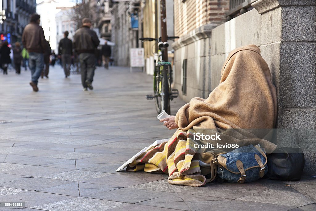Beggar in the street A beggar in the streets of Madrid, holding a cup for donation from passers-by. Homelessness Stock Photo
