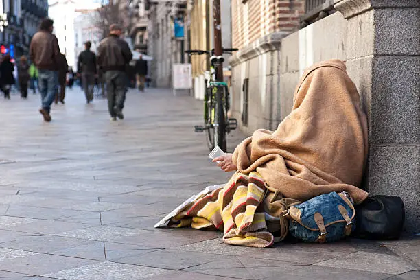 A beggar in the streets of Madrid, holding a cup for donation from passers-by.