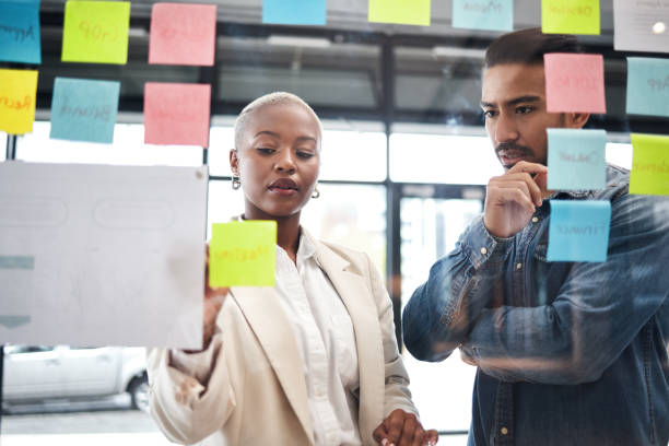 istock Creative people, team and thinking in planning for schedule brainstorming or meeting at office. Man and woman in teamwork decision for project plan, tasks or sticky note ideas in startup at workplace 1554632010