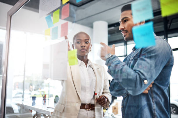 istock Creative people, thinking and meeting for schedule planning, brainstorming or team strategy at the office. Man and woman in teamwork decision for project plan, tasks or sticky note ideas in startup 1554632020