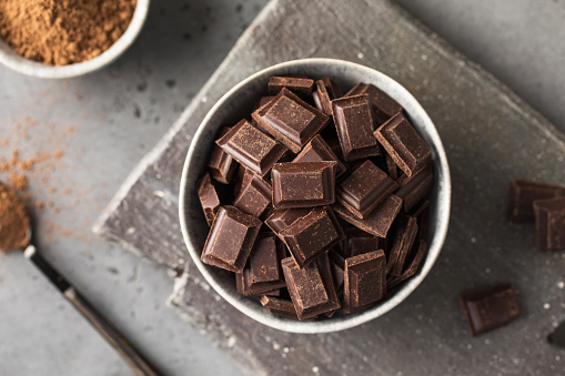 Cocoa powder surrounded by roasted cacao beans and bitter dark chocolate chunks.