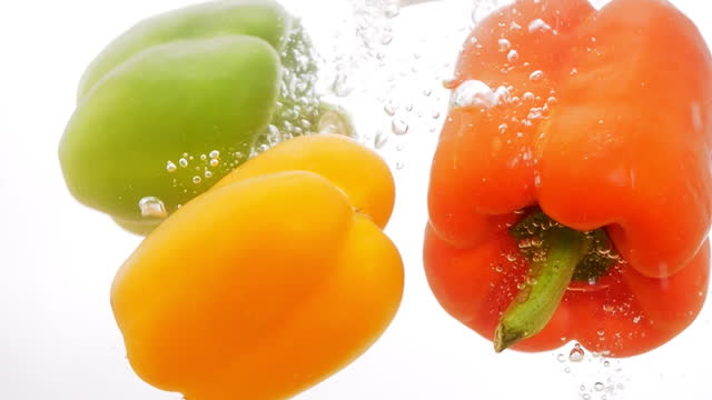 Fresh green, yellow, and red sweet peppers from the farm falling down in water splash on white background.