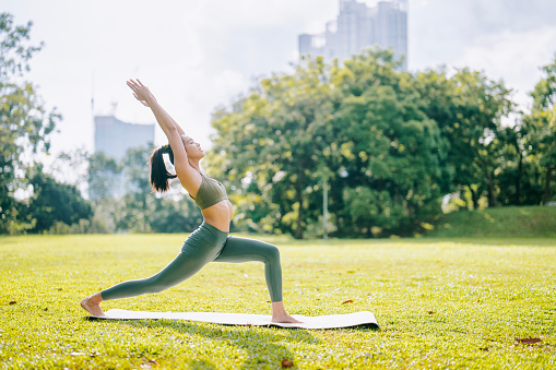 Asian Chinese woman Sun Salutation practicing yoga in public park weekend morning