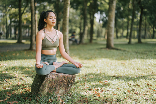 Asian Chinese woman meditating practicing yoga in public park weekend morning