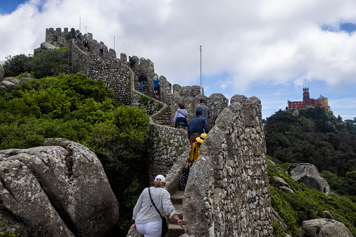 Tourists at Moorish Castle in Sintra, Portugal. Pena Palace in the background.