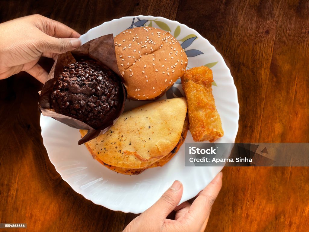 Deferent variety of snacks display on a plate a hand is holding chocolate muffin on wooden background Backgrounds Stock Photo