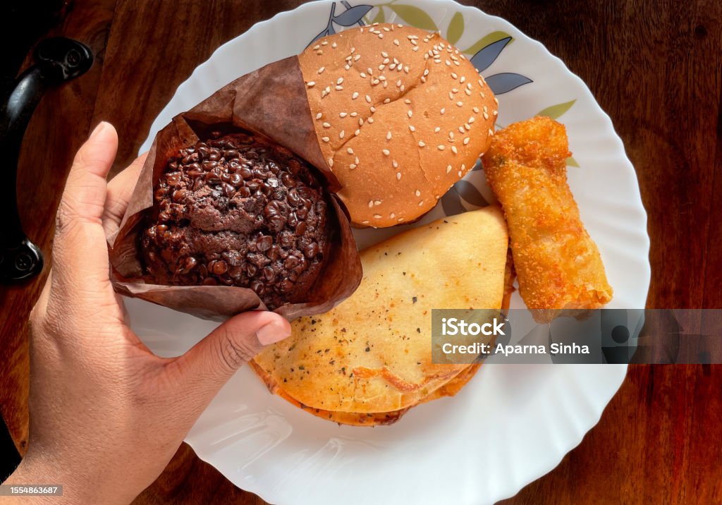 Deferent variety of snacks display on a plate a hand is holding chocolate muffin on wooden background Backgrounds Stock Photo