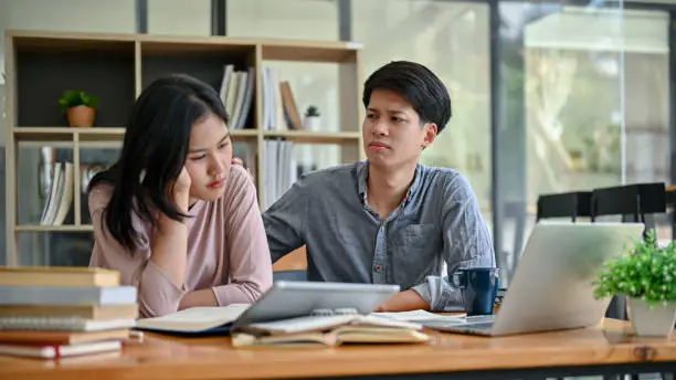 A caring young Asian man is comforting to his upset and stressed-out girl friend while studying and preparing for the exam in a campus library together. expressing sympathy and understanding