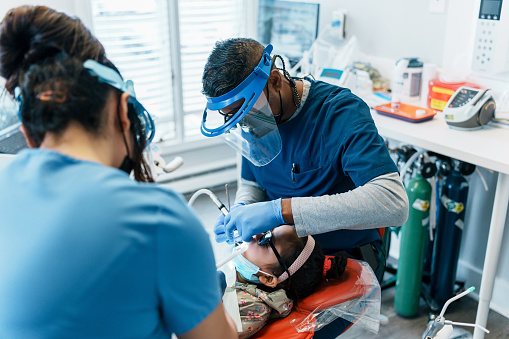 Indian, male dentist and his female dental assistant performs a procedure on a young girl of Asian descent.
