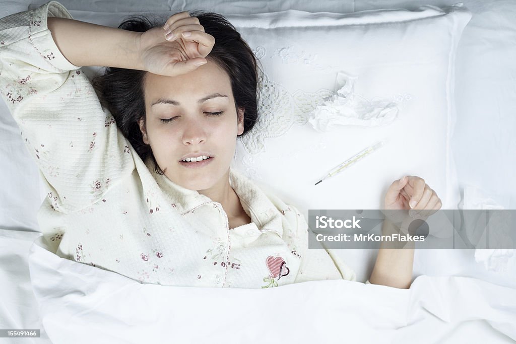 Sick woman in pajamas resting on an all-white bed Ill Woman in Bed with Thermometer and Tissues 20-29 Years Stock Photo