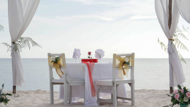 istock Romantic dinner table set and chair preparation with white theme decoration, white sand, clear cloudy sky, and tranquil, peaceful, beautiful beach view at the seashore. Good place for wedding proposal 1554931841
