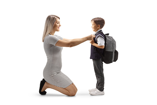Full length profile shot of a mother helping son getting ready for school isolated on white background