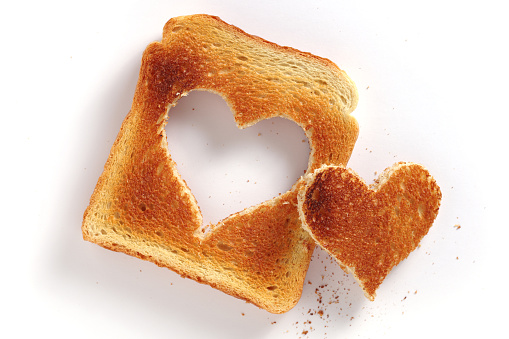 Slice of toasted bread with a cutout in the shape of a heart on white background, top view