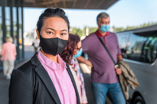 Portrait of an Asian mid adult female arriving to the airport terminal wearing a protective face mask to prevent illness.