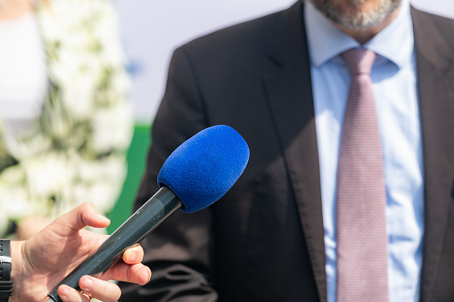 Group of journalists holding microphones standing opposite the speaker and taking an interview