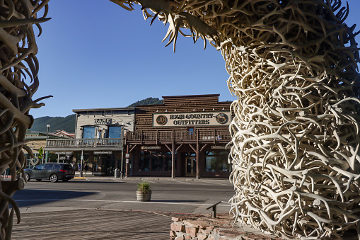 JD High Country Outfitters on East Broadway Avenue of Jackson at Jackson Hole in Teton County, Wyoming. On the right is part of the elk antler arches which adorn the town square. People can be seen in the background.