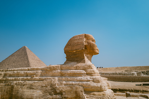 Pyramids of Giza, Giza Necropolis, Egypt - July 14, 2023: Man walking with camels at Great Sphinx of Giza. The Great Sphinx of Giza is a limestone statue of a reclining sphinx, a mythical creature with the head of a human and the body of a lion.