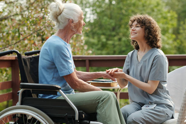 istock Young smiling caregiver in uniform looking at elderly woman with disability 1555086117
