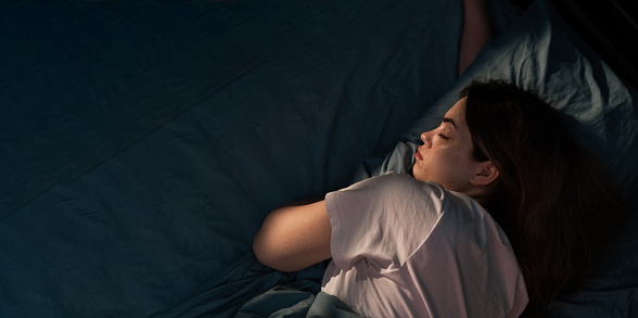 Top view of young woman sleeping in her bed at night. Girl sleeping with closed eyes. Banner, copy space