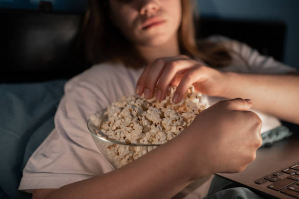 istock Young woman working or watching movie while eating popcorn looking at laptop screen 1555115925