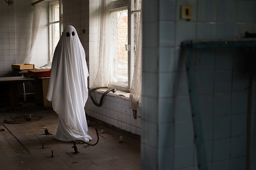 Ghost in white sheet walk in abandoned ruined clinic. Halloween concept
