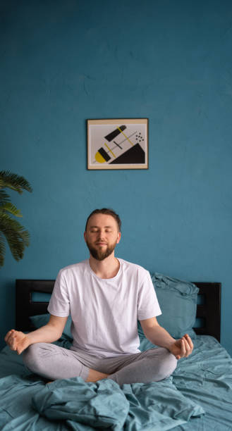 istock Pleased caucasian man with bearded meditating while sitting on bed at bright room 1555117057