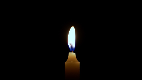 One candle burns with a bright burning flame. An isolated candle burns on a dark background. Paraffin candle is a symbol of remembrance or celebration.