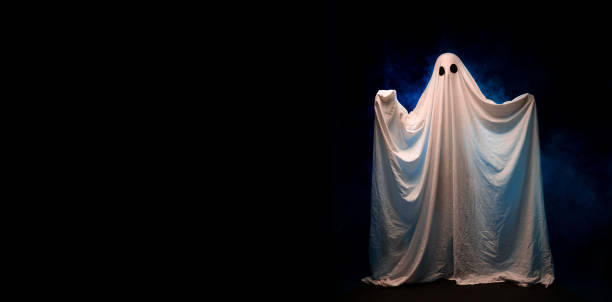 istock A spooky white ghost covered by a sheet with black eyes over dark background in fog. 1555121300