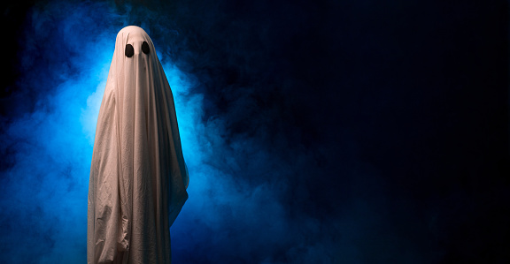 Ghost looking at the camera while standing on a black background with smoke. Copy space. Banner