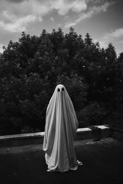 istock Ghost covered with a white ghost sheet on a roof. Black and white photo. 1555121415