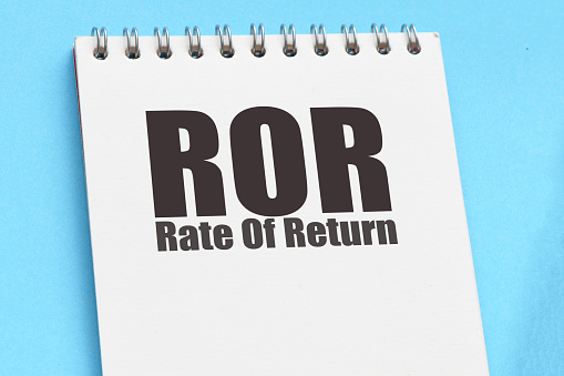 ROR - Rate Of Return words in office notebook next to calculator and calendar.