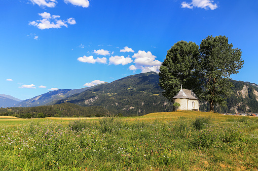 The Sogn Mang chapel at Bonaduz, Grisons on the open field with big lush poplar trees in summer