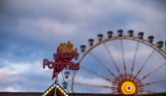 Munich, Germany – April 25, 2023: A closeup shot of an advertisement for food at a carnival in Germany, with a giant ferris wheel in the background