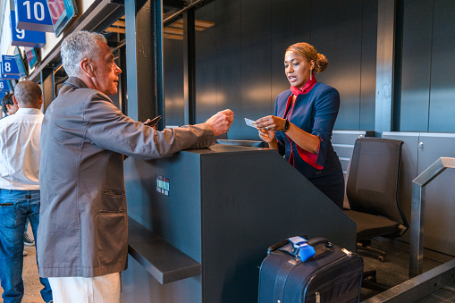 Mid adult Hispanic airline stewardess sitting at a check in counter at the airport. Checking boarding passes.