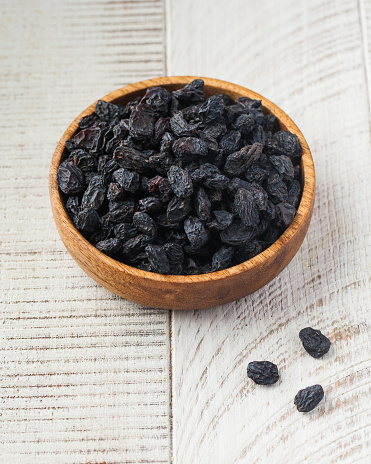 Dark blue raisins in a wooden bowl on a light background. The concept of dried fruits, healthy snacks.