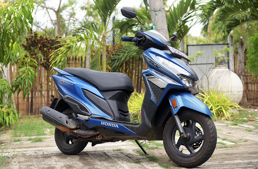 Moped parked by a green bush outside an apartment building