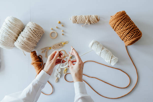 istock Creative hobby handmade macrame for home decoration. Close up of women's hands weaves macrame. Flat lay, top view. 1555236714